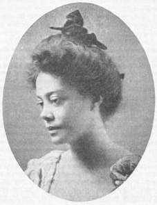 A vintage black and white oval portrait of author Alice Dunbar-Nelson. She has dark hair piled high in a Gibson Girl style and is wearing a light-colored, high-necked blouse.