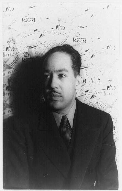 A black and white photograph of a young Langston Hughes. He is handsome and youthful, wearing a suit and tie, looking slightly to the side.
